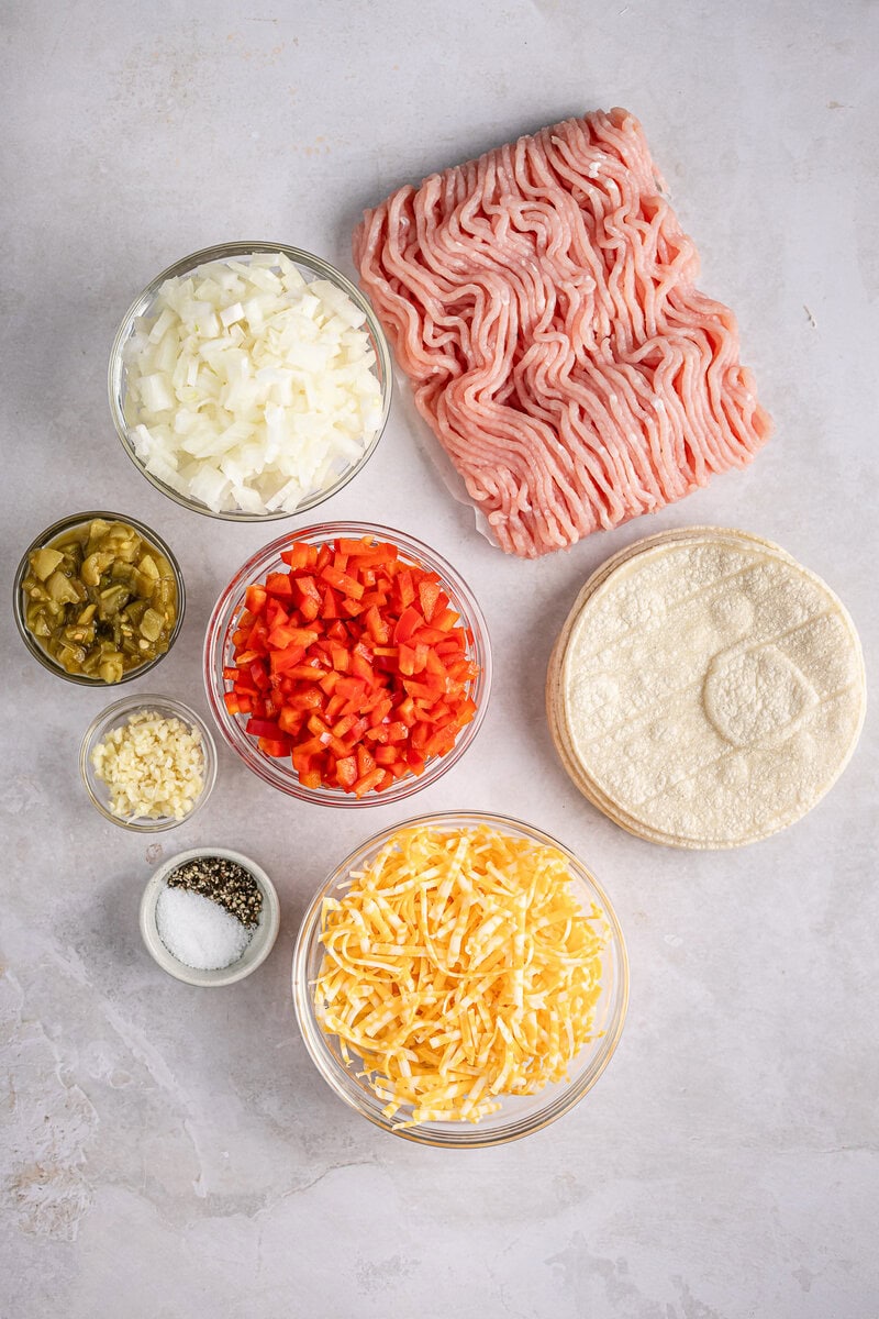 Fresh raw ground beef with diced onions, chopped red bell peppers, shredded cheese, and seasonings on a light background. Ideal ingredients for delicious beef and cheese quesadillas or tacos.