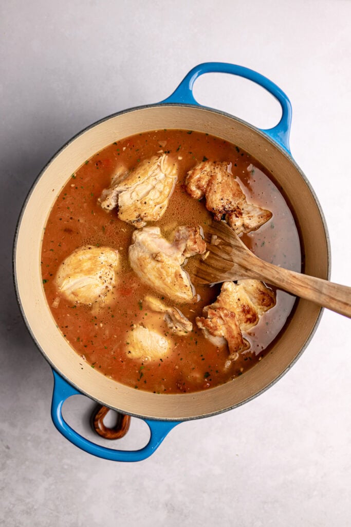 Juicy chicken drumsticks simmering in flavorful broth in a blue French oven.