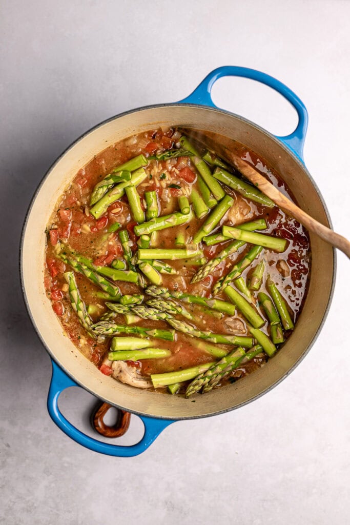 Fresh asparagus cooking in a pot with tomato sauce and herbs, a healthy vegetable dish.