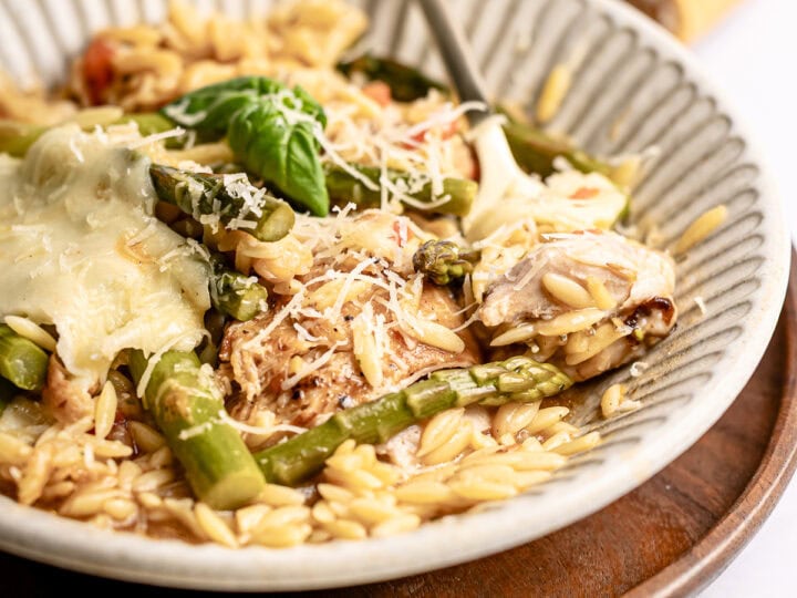 Creamy chicken and vegetable risotto with fresh basil and grated cheese in a textured bowl. Perfect comfort food dish, served on a wooden tray with a breadstick in the background.