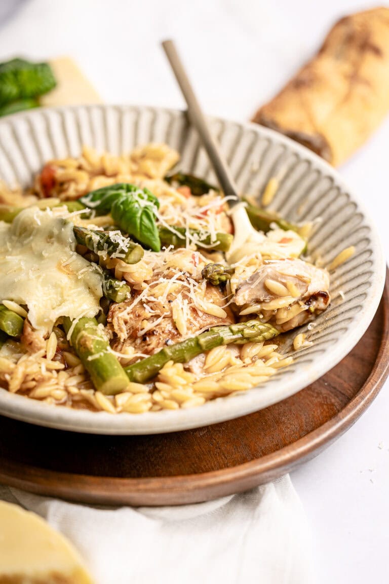 Creamy chicken and vegetable risotto with fresh basil and grated cheese in a textured bowl. Perfect comfort food dish, served on a wooden tray with a breadstick in the background.