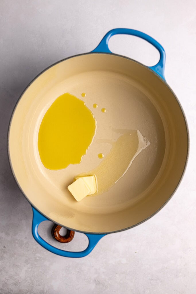 Creamy butter and olive oil melting in a yellow and blue enameled cast iron skillet on a gray surface.