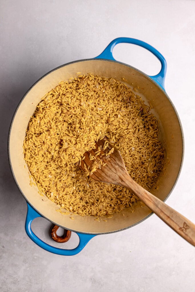 Golden toasted orzo pasta cooking in a pot with a wooden spoon, ready for a savory recipe.