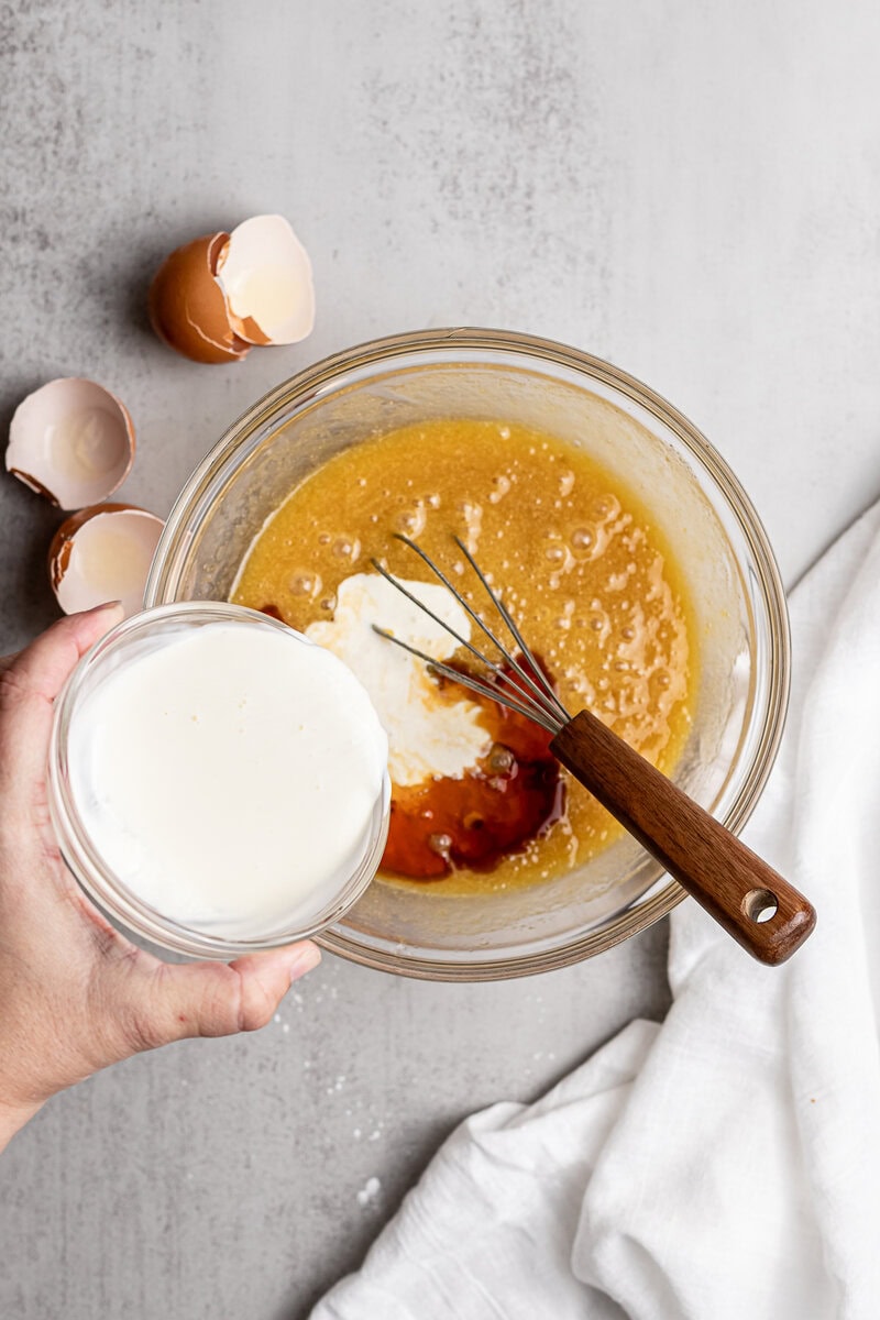 Creamy vanilla and caramel filling being prepared in a glass bowl with eggshells on a light gray surface for sweet dessert recipes.