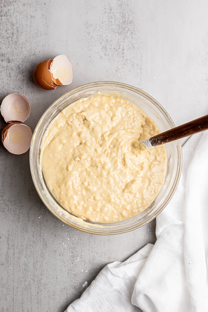 Creamy cake batter in glass mixing bowl with eggshells on gray countertop.