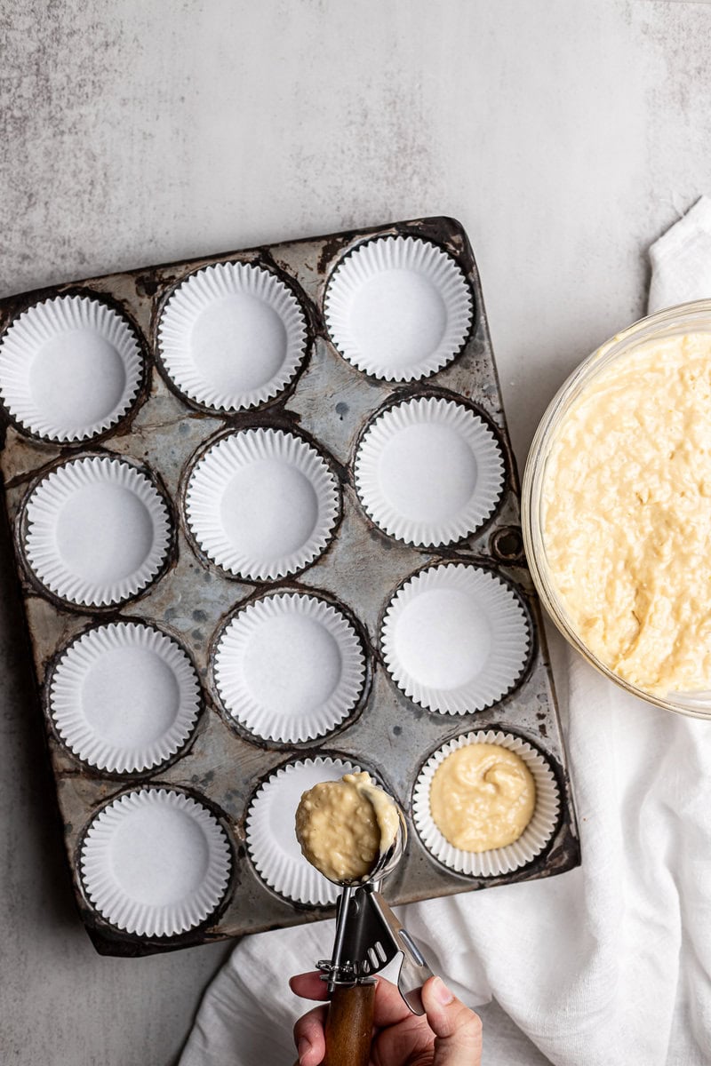 Creamy cupcake batter being scooped into cupcake liners in a metal baking pan for homemade cupcakes.