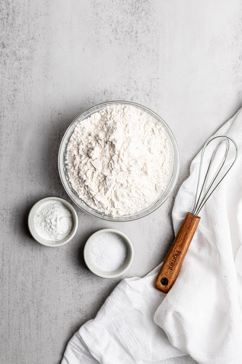 Flour, sugar, and salt in small bowls arranged on a grey surface for baking.