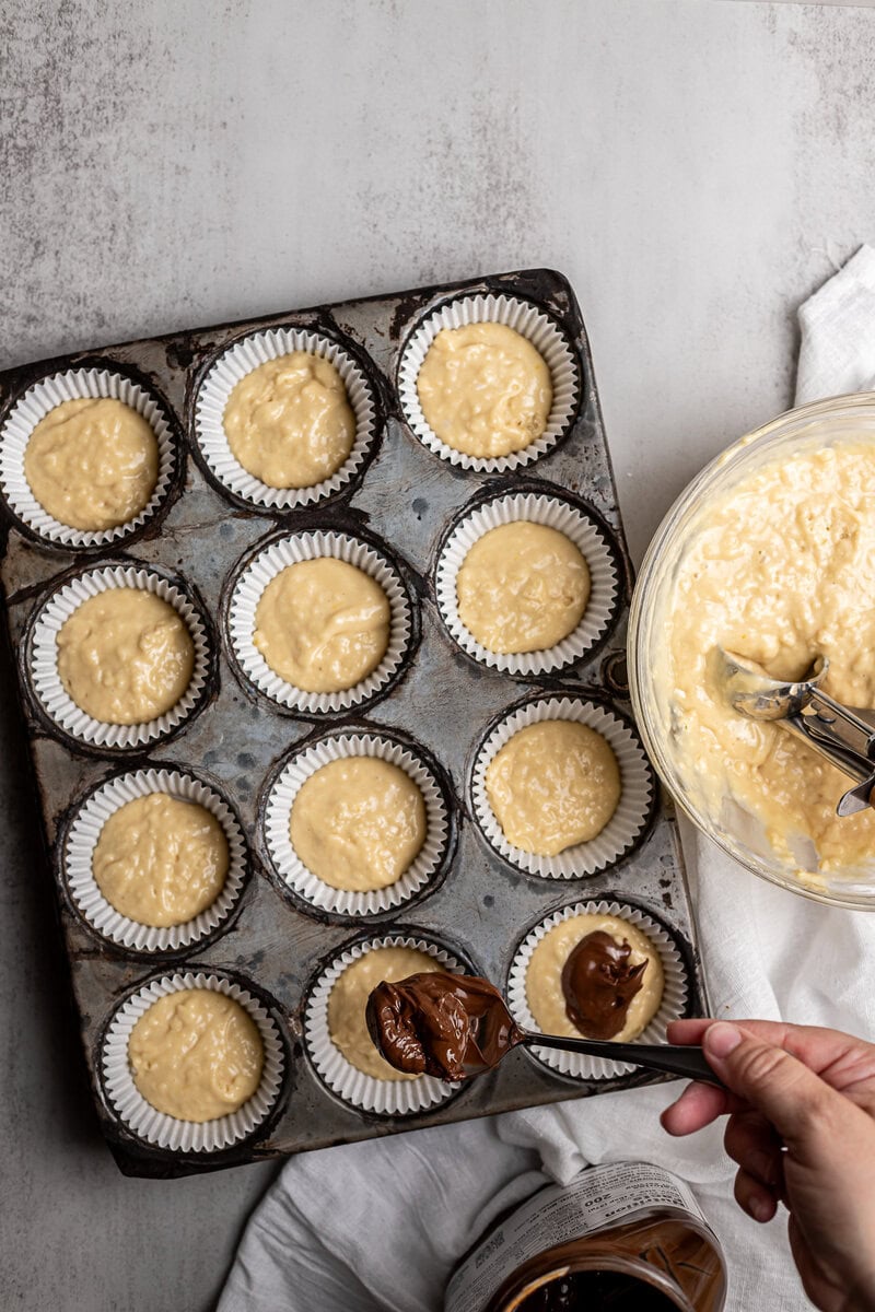 Golden cake batter in cupcake liners ready for baking, with chocolate and caramel toppings being added, on a baking tray with a mixing bowl of batter nearby, perfect for sweet dessert recipes, Stuck On Sweet.