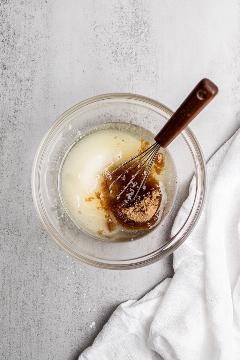 Cream and brown sugar mixture for baking in a glass bowl with a whisk.