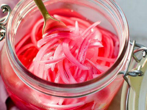 Vegan pickled red onions in a glass jar, ready to serve as a tangy condiment or salad topping. Perfect for adding vibrant color and flavor to meals at Stuck On Sweet.