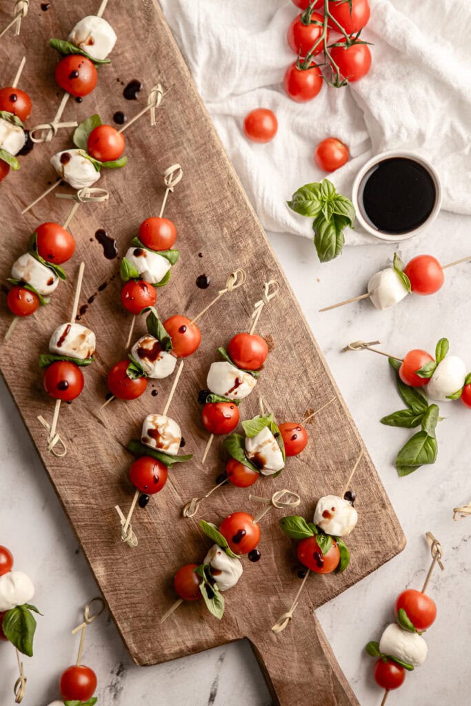 Mini Caprese Skewers with Cherry Tomatoes, Fresh Mozzarella, Basil, and Balsamic Drizzle on Wooden Board - Perfect Appetizer for Parties and Gatherings.