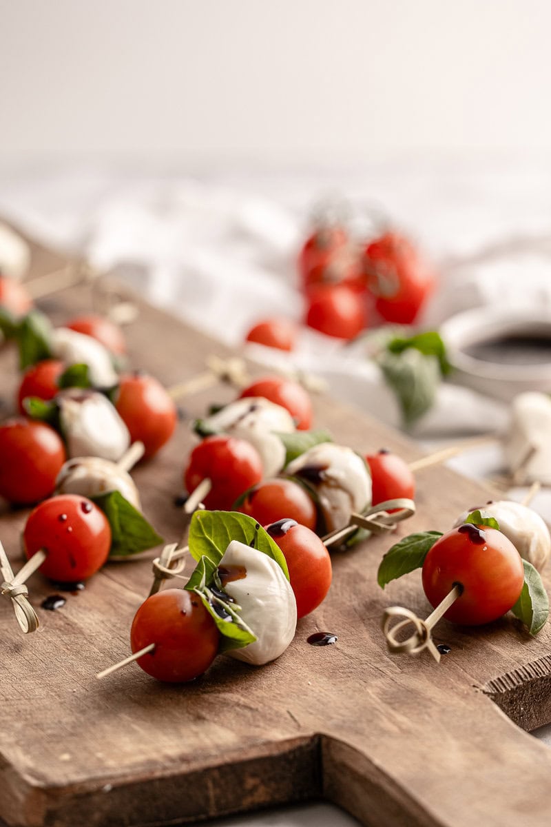 Cherry Caprese Skewers with Fresh Mozzarella, Basil, and Balsamic Drizzle on Wooden Serving Board for Appetizer or Party Snack.