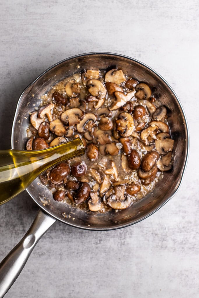 Sautéing sliced mushrooms in a stainless steel pan with olive oil for a delicious homemade mushroom dish. Perfect for mushroom lovers and easy to prepare for any meal.