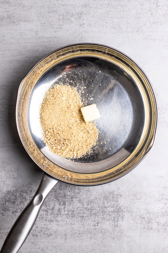 Golden graham cracker crumbs and a pat of butter in a stainless steel mixing bowl for crumb crust preparation.