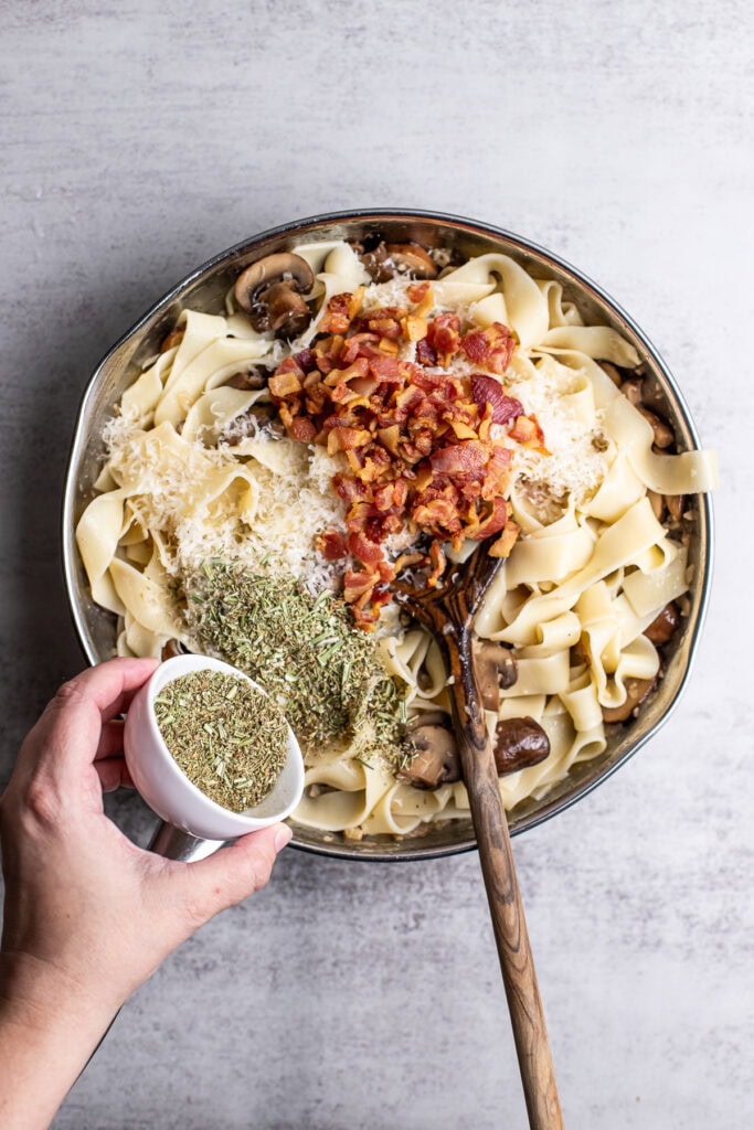 Creamy mushroom and bacon pasta with herbs in a mixing bowl, close-up, top view.