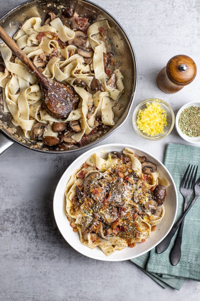Creamy mushroom and bacon fettuccine pasta dish with grated cheese, herbs, and seasonings, perfect for a comforting homemade meal.