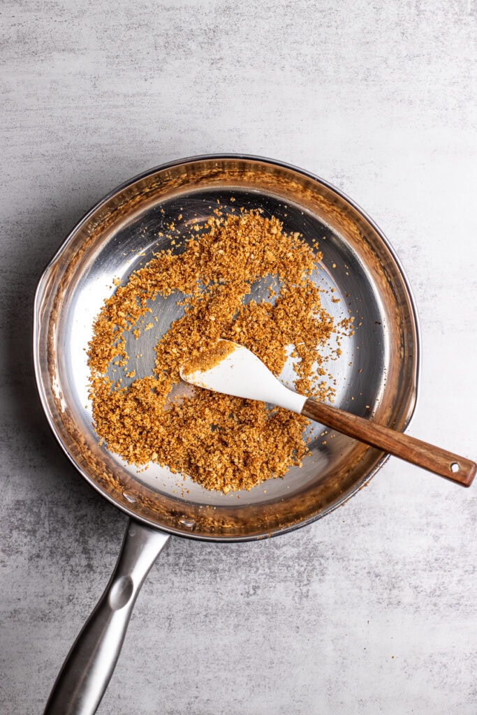 Crunchy graham cracker crumbs in a stainless steel skillet for baking or dessert topping.