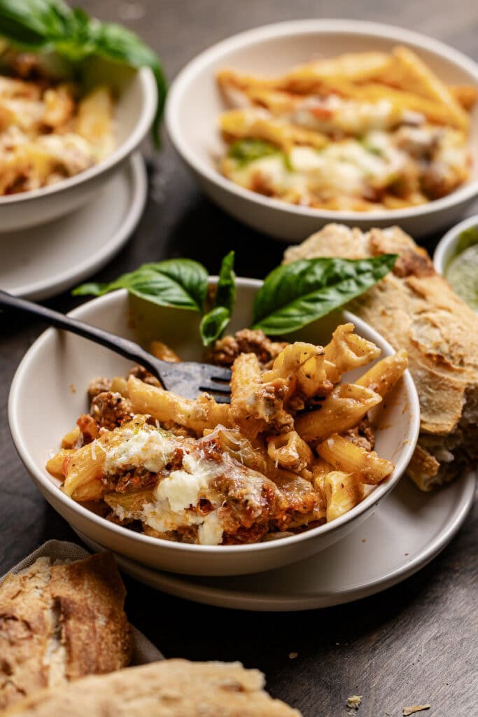 Rich, cheesy baked pasta with ground beef, fresh basil garnish, served with crispy breadsticks and side dips, perfect for comfort food lovers.