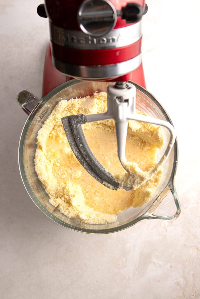Creamy vanilla cake batter in a glass mixing bowl with a red stand mixer, ready for baking, perfect for homemade cake recipes from Stuck On Sweet.