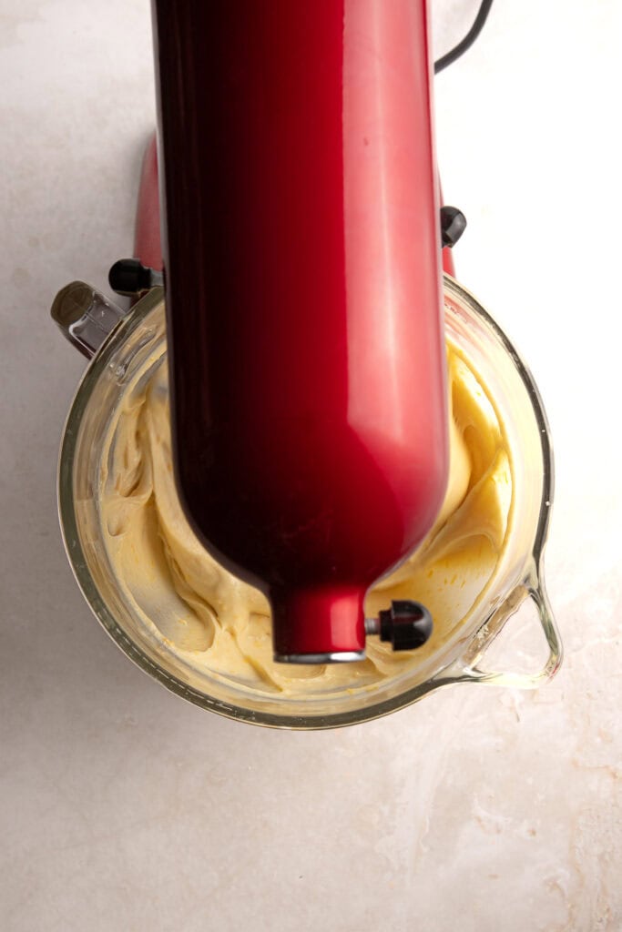 Cream cheese frosting being mixed with an electric hand mixer in a glass bowl.
