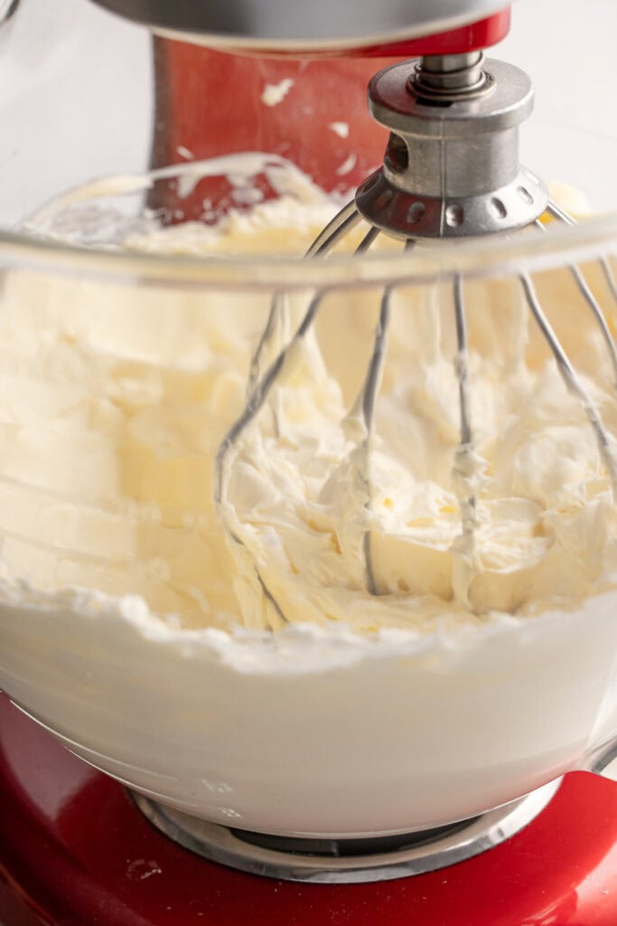 Smooth creamy butter being mixed with an electric mixer in a clear glass bowl on a red stand mixer.