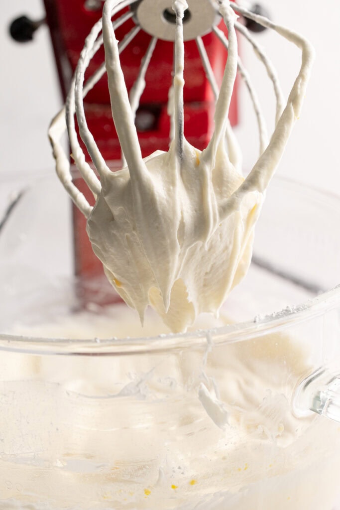 Fluffy white cake batter on a mixer paddle during baking preparation.