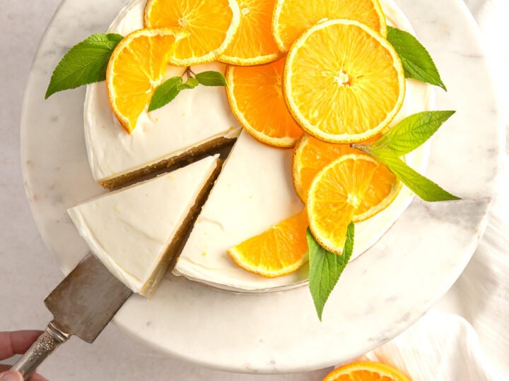 Fresh orange slices on a creamy cheesecake topped with mint leaves, served on a marble cake stand, perfect for citrus-inspired desserts.