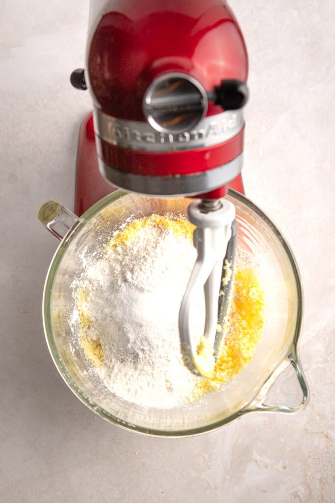 Bright red stand mixer mixing flour and sugar in a glass bowl for baking.
