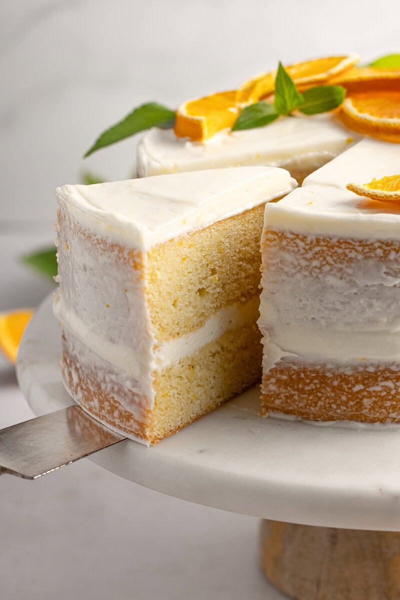 Light vanilla layer cake with orange slices and fresh mint garnish, topped with smooth white frosting, perfect for citrus-inspired dessert lovers.
