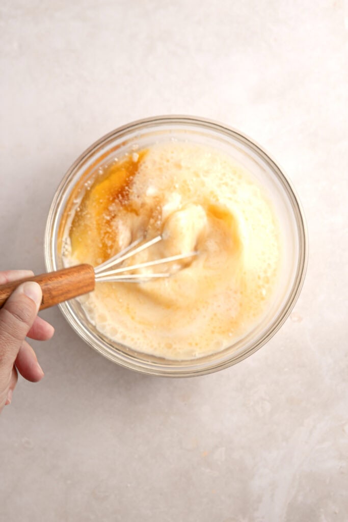 Creamy homemade custard being whisked in a glass mixing bowl for baking or dessert recipes.