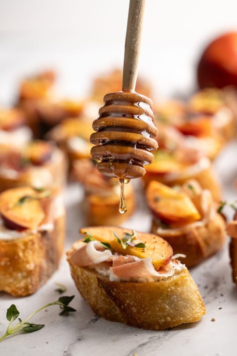 Sweet honey drizzled over savory Bruschetta appetizers with fresh herbs and peaches on toasted baguette slices, perfect for snacks or parties.