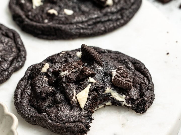 Rich chocolate cookies topped with Oreo pieces on a white marble surface. Perfect for dessert lovers and cookie enthusiasts. Highly indulgent, chocolate cookies with creamy white chocolate chunks.