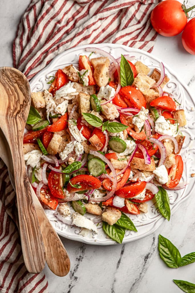 Fresh Tomato Caprese Salad with Basil, Red Onion, and Croutons on a White Plate.