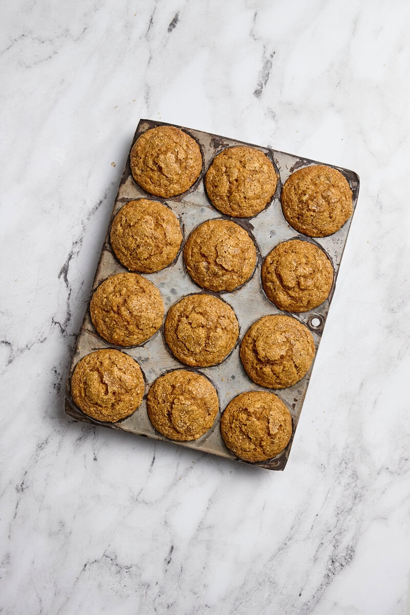 Golden brown homemade cookies arranged on a baking sheet with parchment paper on a white marble surface.