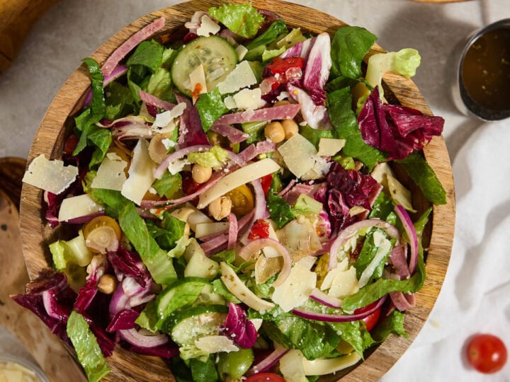 Fresh garden salad with mixed greens, cherry tomatoes, cucumbers, shredded cheese, and vinaigrette, served in a wooden bowl. Perfect for healthy, flavorful meals and side dishes.