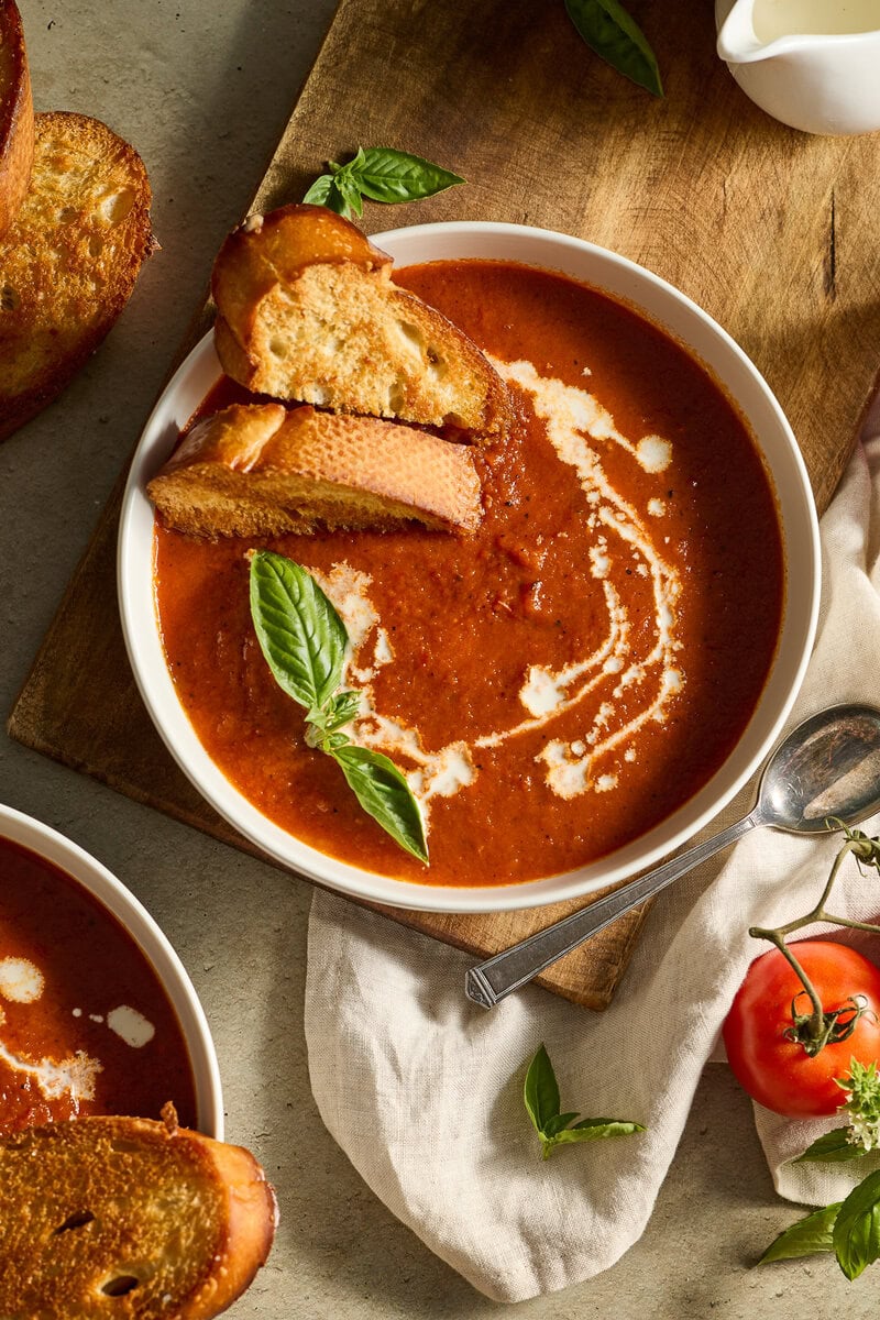 Creamy tomato basil soup with fresh basil leaves and garlic bread on a rustic wooden table.