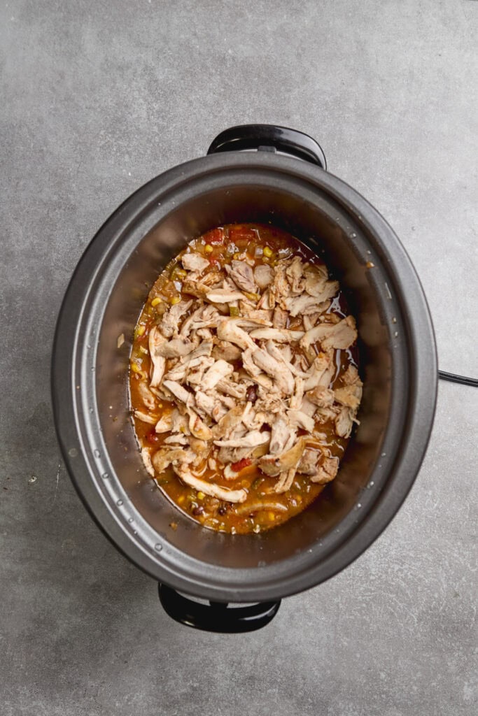 shredded chicken being added to a slow cooker of chicken tortilla soup