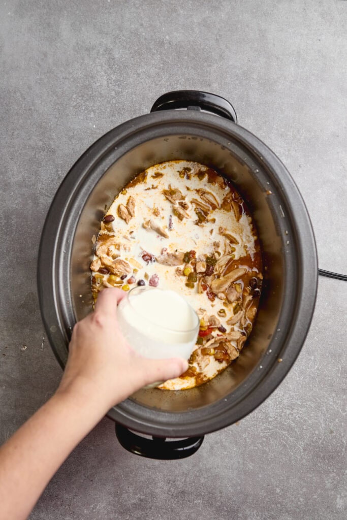 cream being added to a slow cooker of chicken tortilla soup