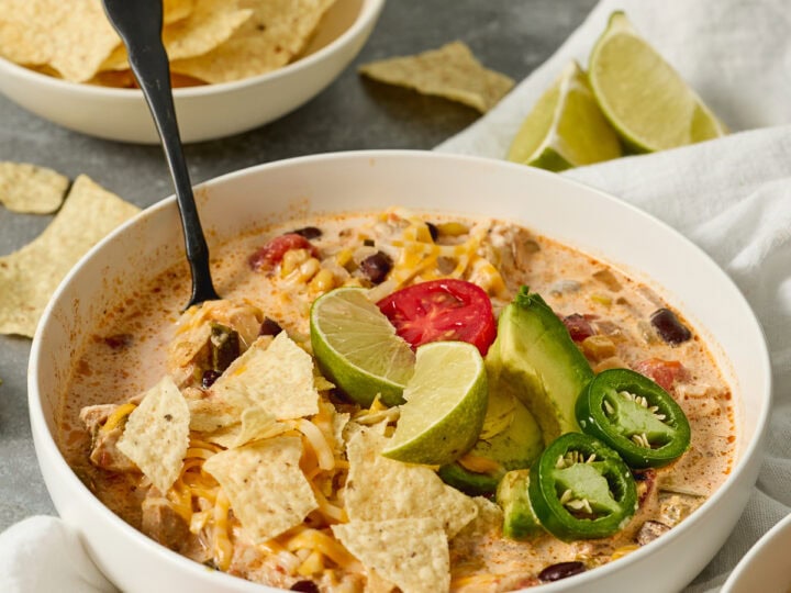 Creamy Mexican chicken tortilla soup garnished with lime wedges, jalapeños, and tortilla chips for a flavorful comfort food meal.