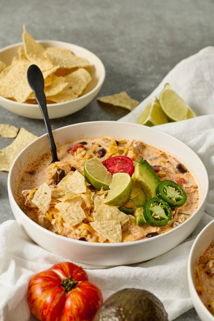 Creamy Mexican chicken tortilla soup garnished with lime wedges, jalapeños, and tortilla chips for a flavorful comfort food meal.