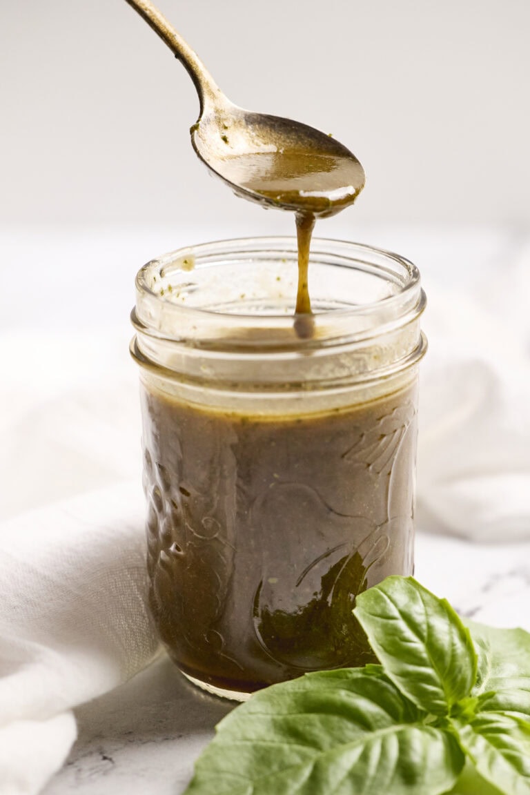 Silky chocolate fudge sauce being spooned into a glass jar, with fresh basil leaves in the foreground, perfect for dessert toppings or baking.