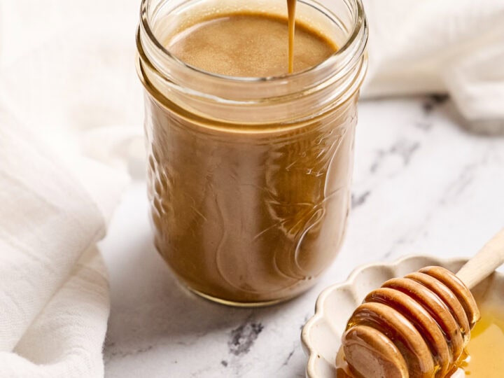 Creamy salted caramel sauce in a jar with honey drizzled on honey dipper, perfect for desserts, sweet treats, and recipes at Stuck On Sweet.