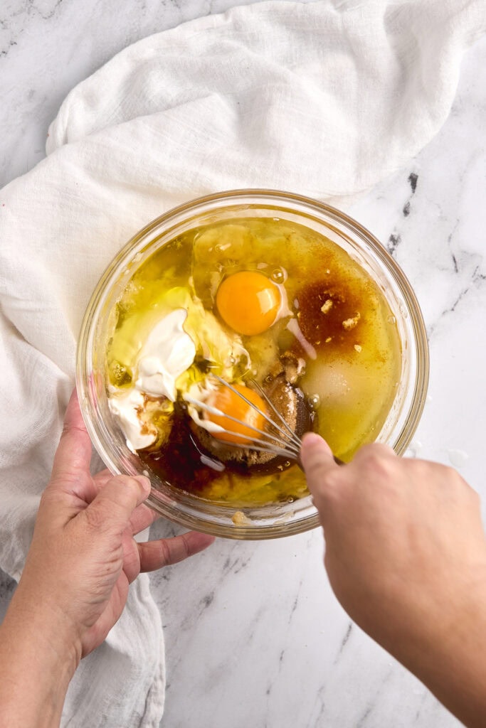 Bright mixing bowl with eggs, vanilla, and spices for baking, on a marble surface with a white cloth.
