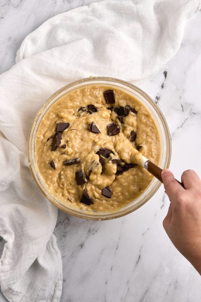 Creamy cookie dough with chocolate chunks in a glass bowl over a white marble surface.