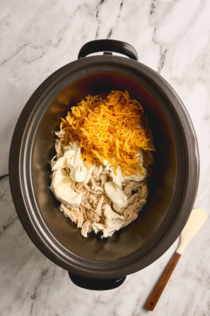 Shredded cheddar cheese, cream cheese, and shredded cooked chicken in a slow cooker for delicious chicken casserole recipe.