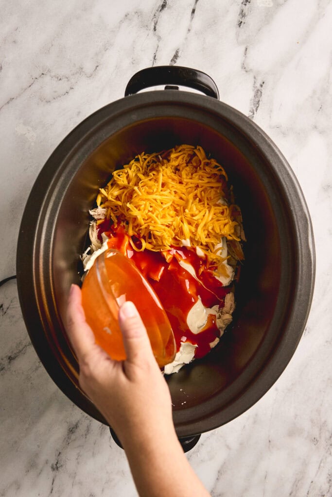 Shredded cheddar cheese, barbecue sauce, and shredded cooked chicken in a slow cooker for a delicious hot chicken dip. Perfect for parties and easy snack recipes from Stuck On Sweet.