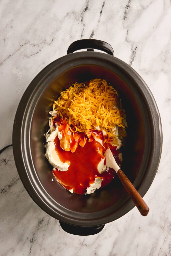 Shredded cheddar cheese, mayonnaise, and barbecue sauce in a slow cooker, ingredients for a cheesy barbecue chicken dip. Perfect for parties and snack time.