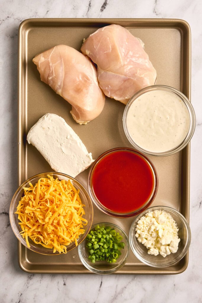 Slow Cooker Buffalo Chicken Dip Ingredients -Juicy chicken breasts, creamy cheese, and flavorful ingredients for a delicious cooked dish in a baking tray.