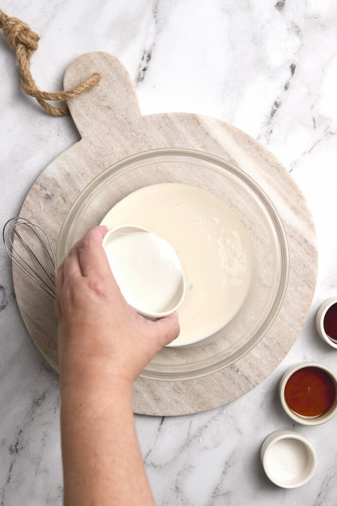 Cream being added to a mixing bowl for dessert recipe on marble surface.