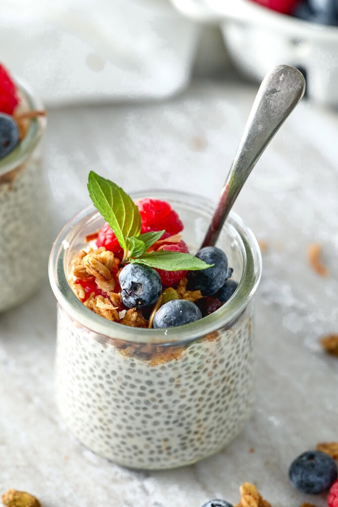 Fresh blueberry chia pudding topped with granola, raspberries, and mint leaves. Perfect healthy breakfast or snack by Stuck On Sweet. Keywords: chia pudding, blueberries, healthy snack.
